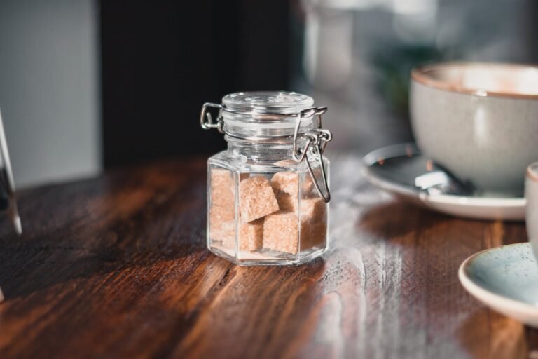 Clear Condiment Shaker With Brown Sugar Cubes Near Gray Teacup